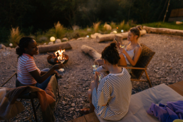 3 women sitting around a campfire drinking wine at dusk