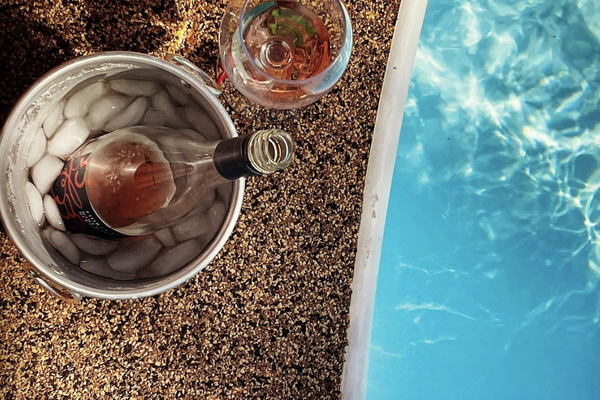 A bottle of rosÃ© in an ice bucket beside a blue pool