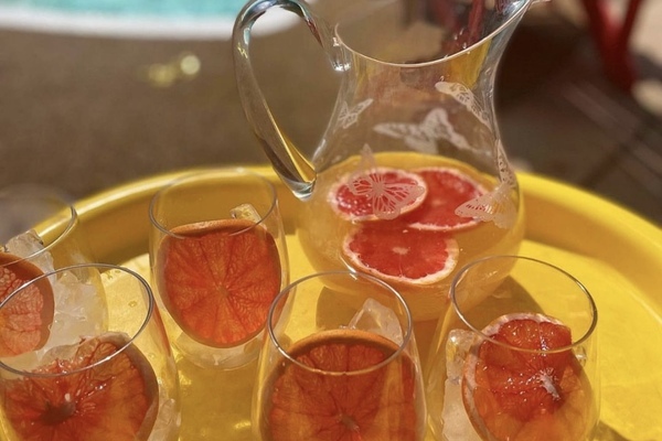 a pitcher of cocktail with grapefruit sitting beside a pool on a sunny day