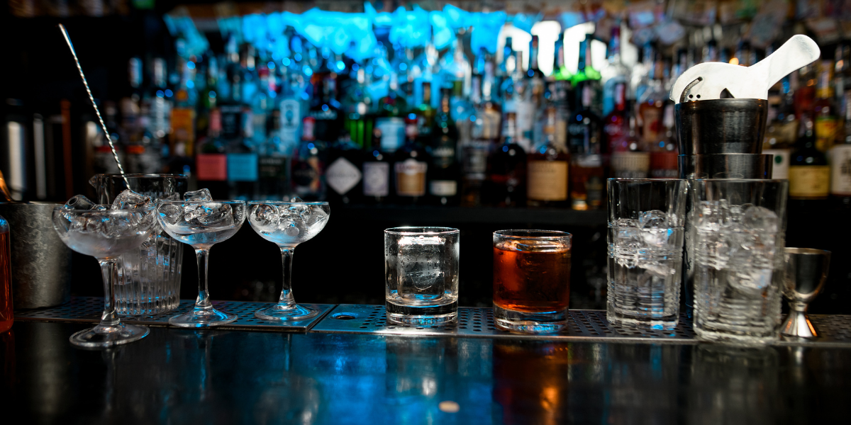 a dark bar with a line of glassware, shakers, and barspoons