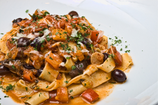 A close up of puttanesca pasta against a white background