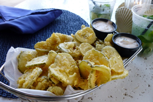 a bowl of fried pickles beside a smaller white bowl of ranch