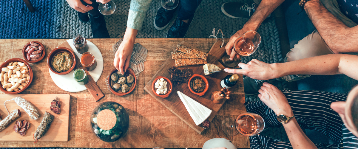 a casual lay out of cheese, charcuterie and wine with a group of people around the table
