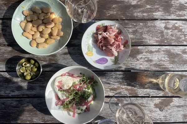 A series of bowls and plates with cheese, charcuterie, olives on a rustic wooden table in the sun