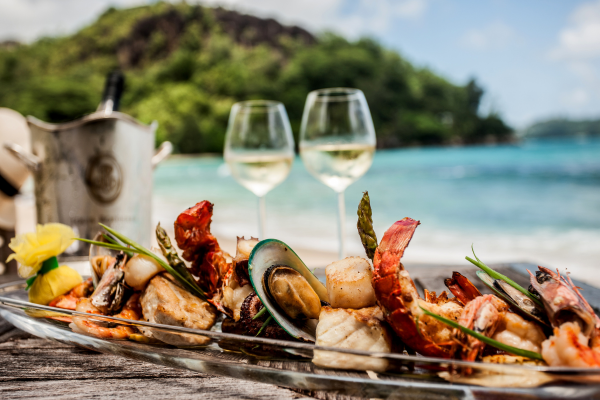 a mixed platter of seafood beside two glasses of white wine and a bottle in a bucket filled with ice, on a beach