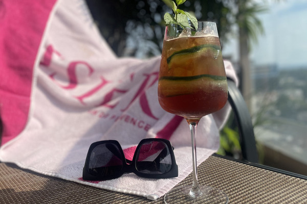 A Pimm's cup, with mint and cucumber, sitting on a lawn chair with a beach towel and sunglasses in the background