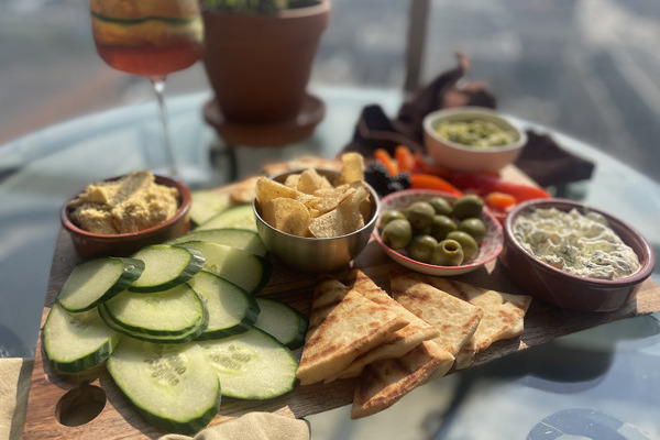 a wood board overflowing with bread, vegetables, olives and three different dips, on a patio table