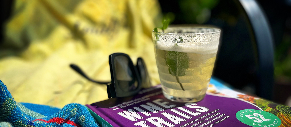 A tumbler of scroppino on a wine book on a beach blanket, wine book and sunglasses in background