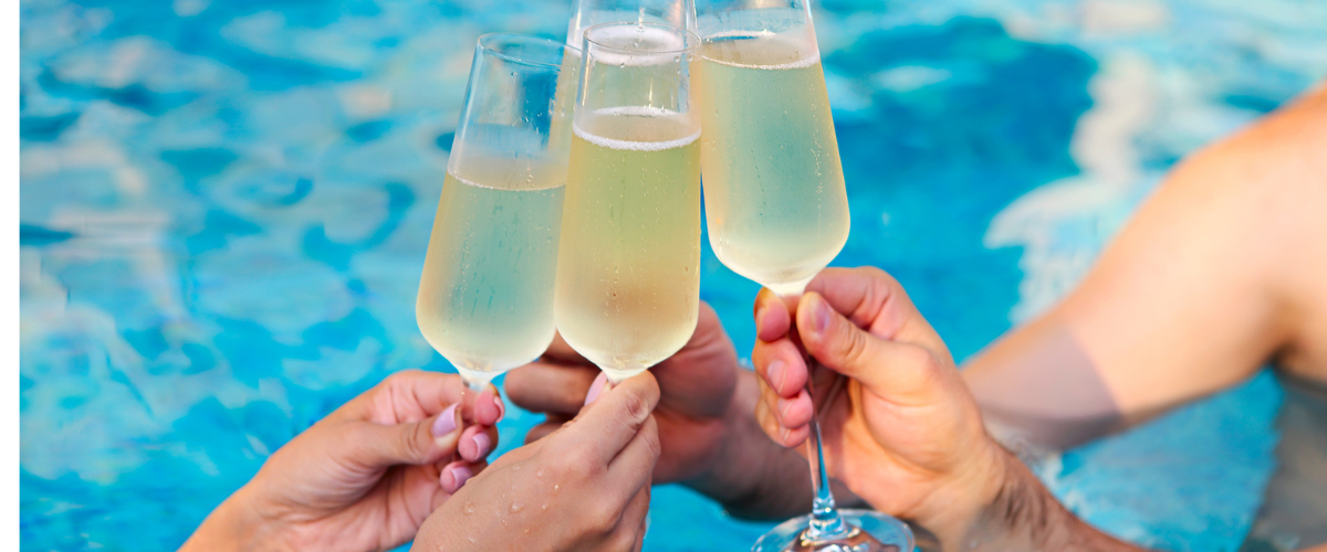 four champagne glasses clinking together in front of a blue pool