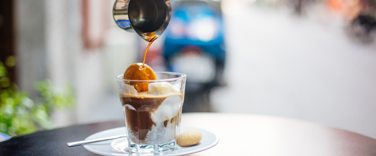A glass tumbler with vanilla ice cream, a hot espresso pouring into it