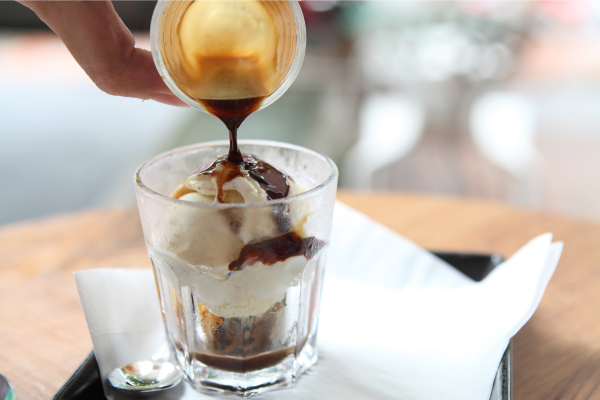 A glass tumbler with vanilla ice cream, a hot espresso pouring into it