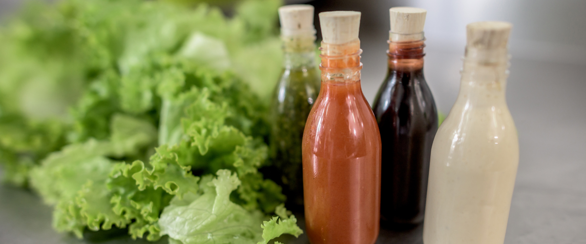 four bottles of differently coloured salad dressings beside a head of leafy, green lettuce