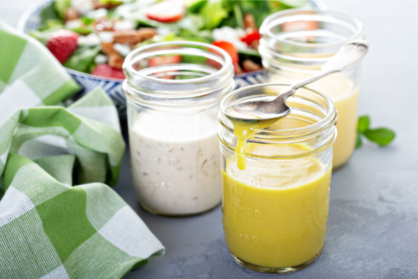 three jars of salad dressing, in the background a bowl of salad