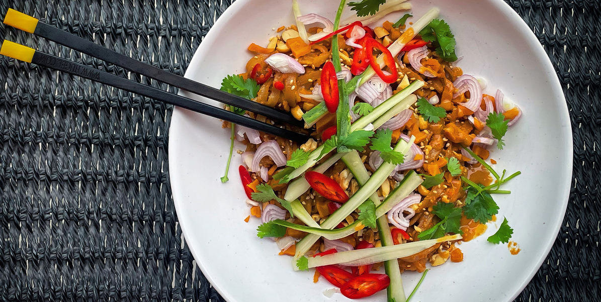 A white bowl filled with noodles and colourful vegetables, black chopsticks sticking out of the side