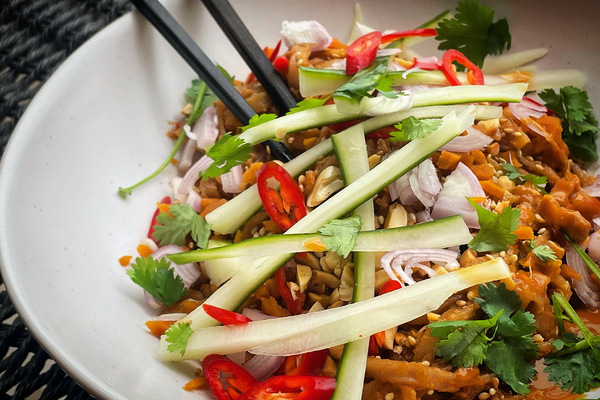 A white bowl filled with noodles and colourful vegetables, black chopsticks sticking out of the side