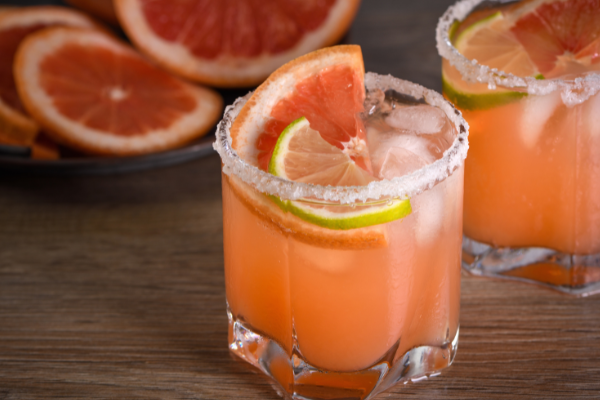 a glass of a pink paloma on a wood bar