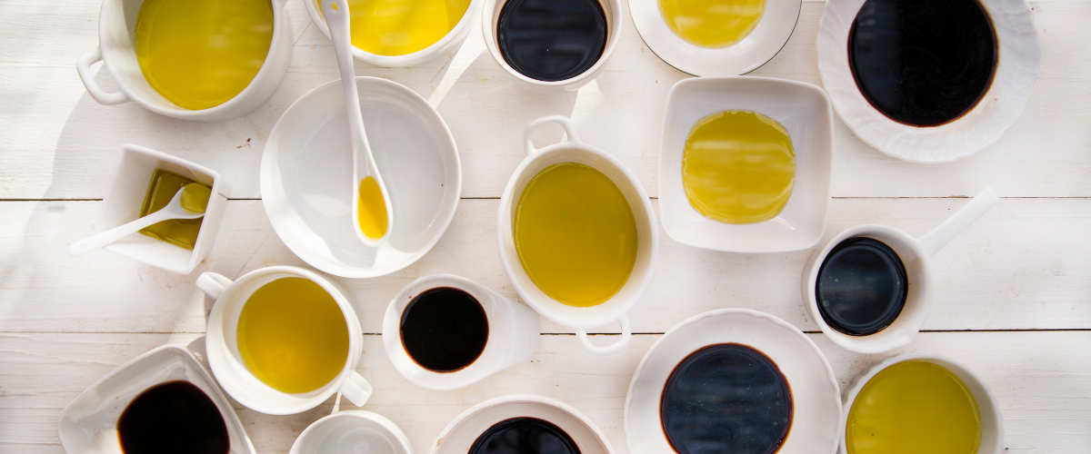 top view of numerous bowls of different sizes filled with oil or vinegar on a white wood-plank table