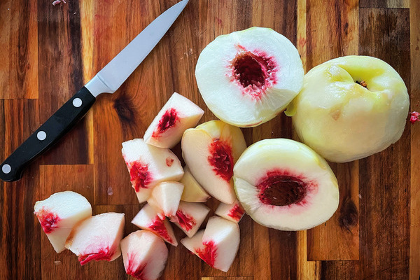 peeled white peaches cut open on a wood board, a knife beside them