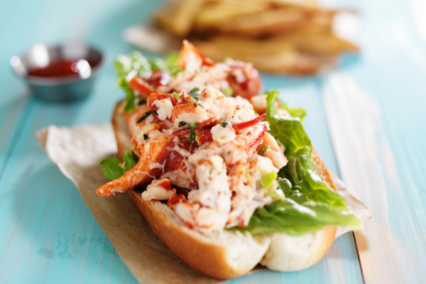 A lobster roll on butcher paper; blurry fries and ketchup in the background