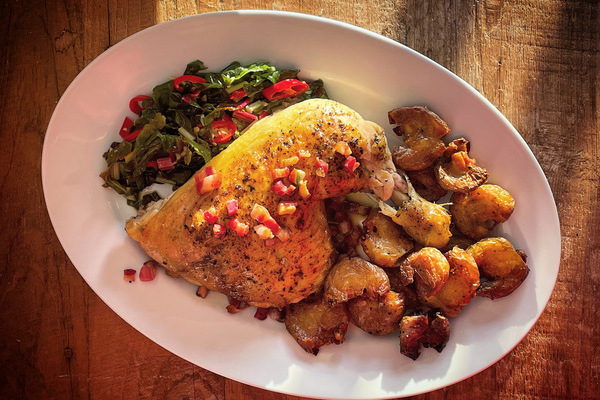 A chicken leg in the centre of a white serving plate, crispy potatoes to one side, sautÃ©ed Swiss chard on the other.