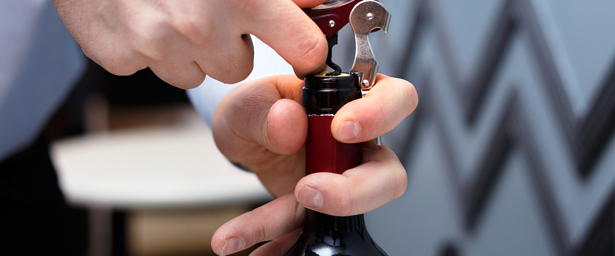 A close up on a man's hands using a waiter's corkscrew to open a bottle of wine