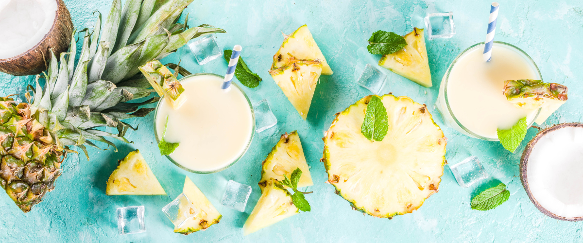 overhead view of a scattering of pina colada drinks, pineapples and tropical notes on a turquoise table