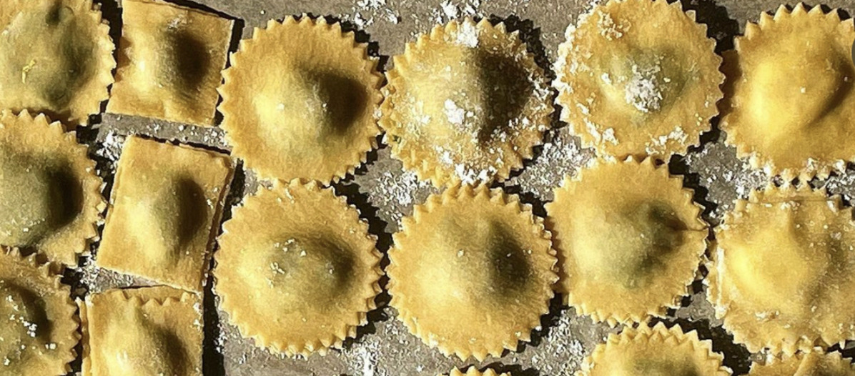 A sheet of stuffed pasta in round and square shapes with sunlight streaked across them
