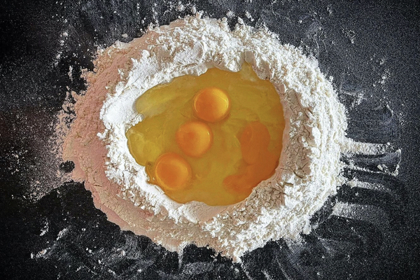 A pile of flour on a black surface, four eggs cracked into the centre of the flour
