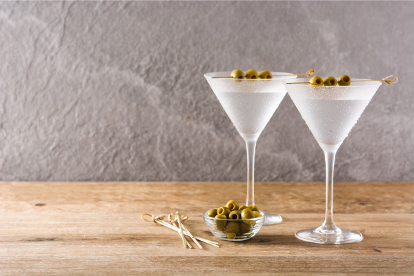 two martinis in coups with olives sitting on a bar