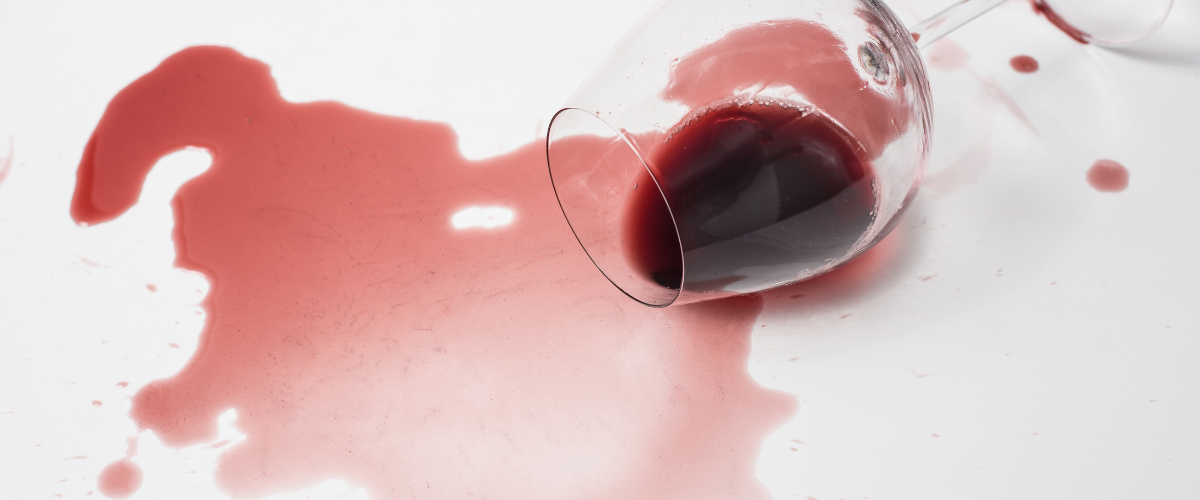 A glass of red wine knocked over and spilled across a white surface