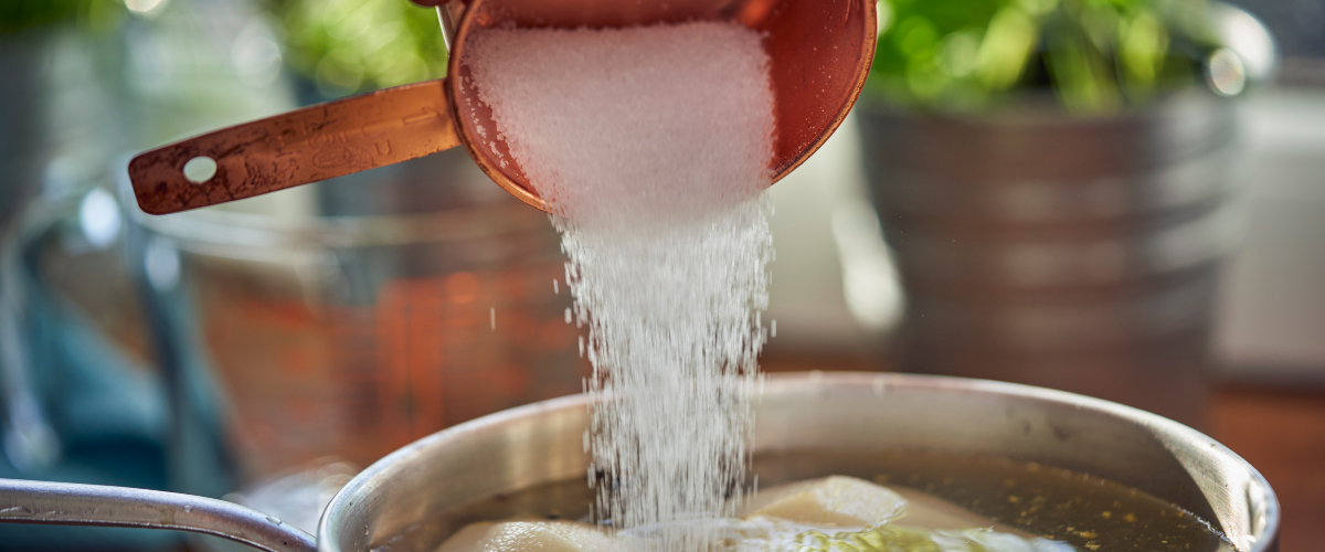Close up of a copper measuring cup pouring white sugar into a pot