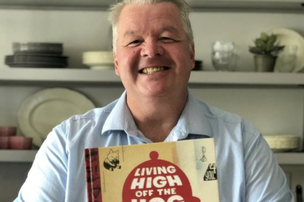 Chef Michael Olson smiling and holding his book, Living High Off the Hog