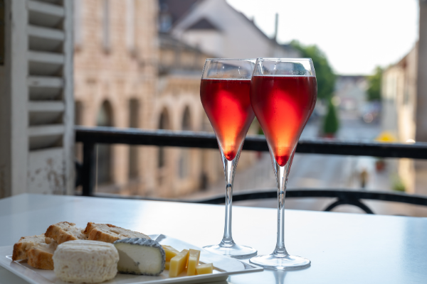 two flutes filled with red sparkling wine in the window of an unidentified European city beside a cheese plate