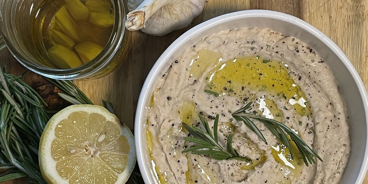 white bean dip in a bowl with garlic oil and rosemary