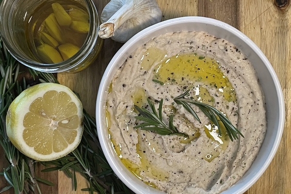 bowl of white bean dip with rosemary garnish, lemon and garlic off to the side