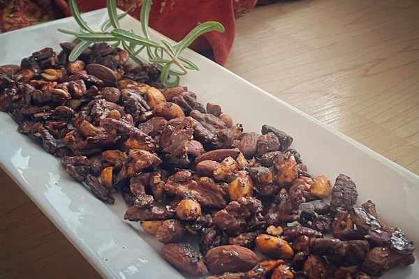 a white plate filled with roasted mixed nuts and a sprig of rosemary