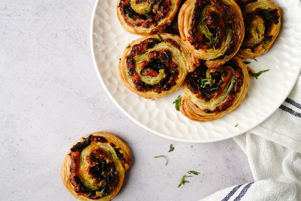 An overhead image of puff pastry pinwheels on a cake stand, one sitting on a white marble counter beside it. Thyme scattered around and a rumpled kitchen towel off to the side.