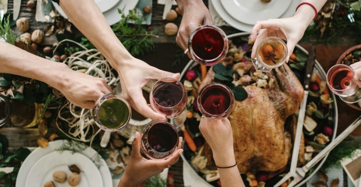4 glasses clinking above a roast turkey and table set for the holidays