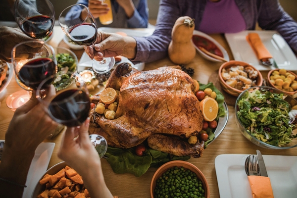 4 glasses clinking above a roast turkey and table set for the holidays