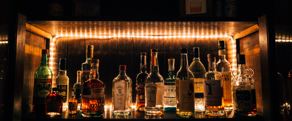 A very dark bar, dimly lit by twinkle lights, unidentified bottles sitting on a shelf