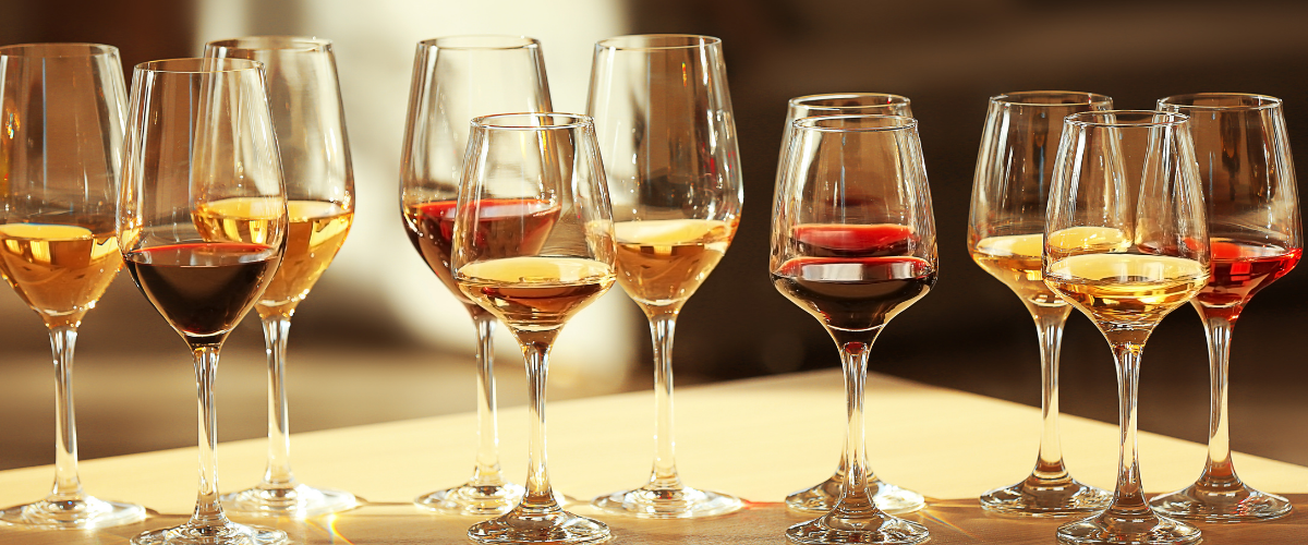 Several differently sized wine glasses with different colours of wines in a row