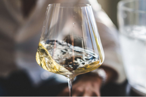 A large glass of white wine swirling; the blurry image of a man in the background