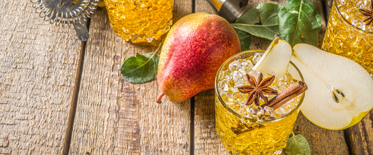 overhead view of yellow drinks in etched crystal tumblers garnished with star anise spice and cinnamon. Red pears surround the drink.