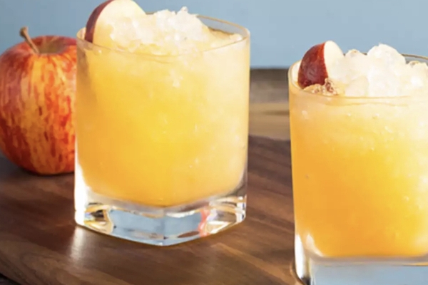 Two cocktail glasses with apple cider sour and an apple in the background