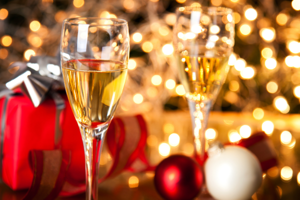 two glasses of white wine against a twinkle light background, red and white tree ornaments around the glasses