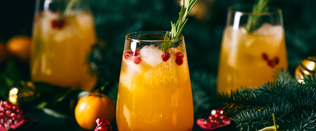 3 orange cocktails in low ball glasses with greenery and oranges surrounding them