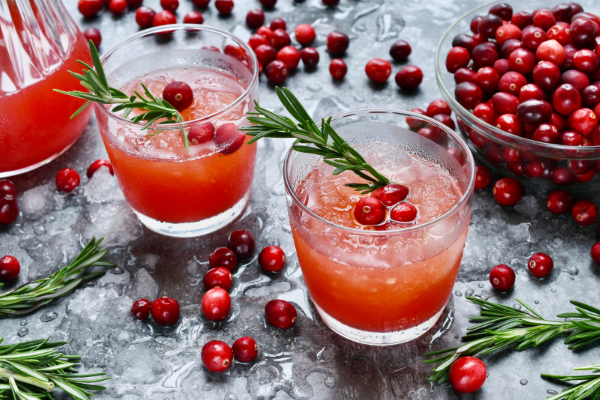 Two red drinks on rocks glasses, cranberries and rosemary garnishing the drinks and scattered about