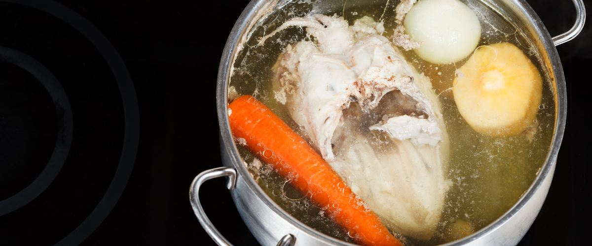 top view of a pot of stock containing turkey, root vegetables and herbs