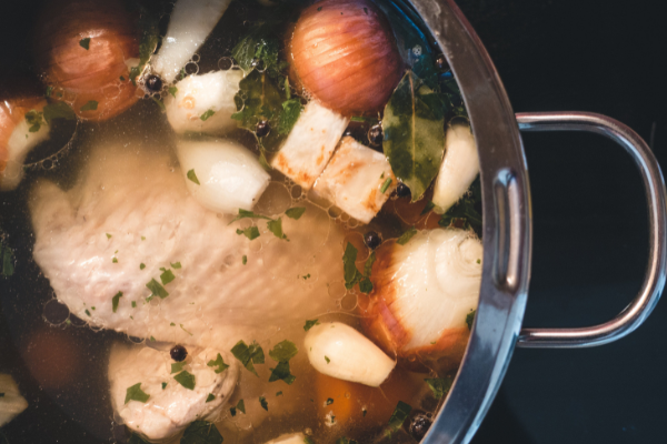 top view of a pot of stock containing turkey, root vegetables and herbs
