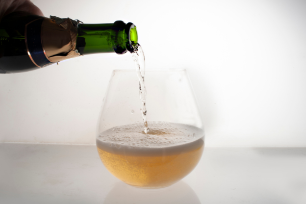 a stemless wine glass against a lit-up white background, sparkling wine being poured into it a foaming up